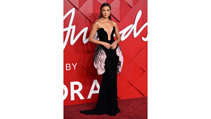 Olivia Culpo poses on a red carpet in a plunging black figure-hugging gown.